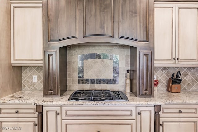 kitchen featuring cream cabinetry, stainless steel gas stovetop, light stone counters, and tasteful backsplash