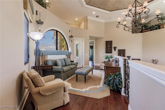 living room with dark wood-type flooring, a chandelier, crown molding, a raised ceiling, and a high ceiling