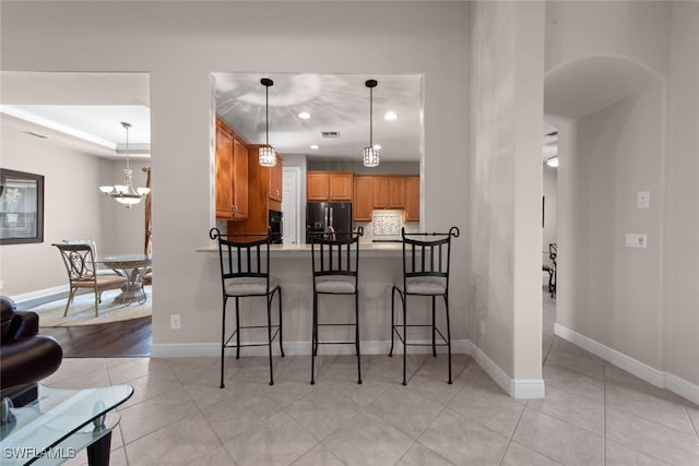 kitchen featuring arched walkways, light tile patterned floors, a breakfast bar, baseboards, and black refrigerator with ice dispenser