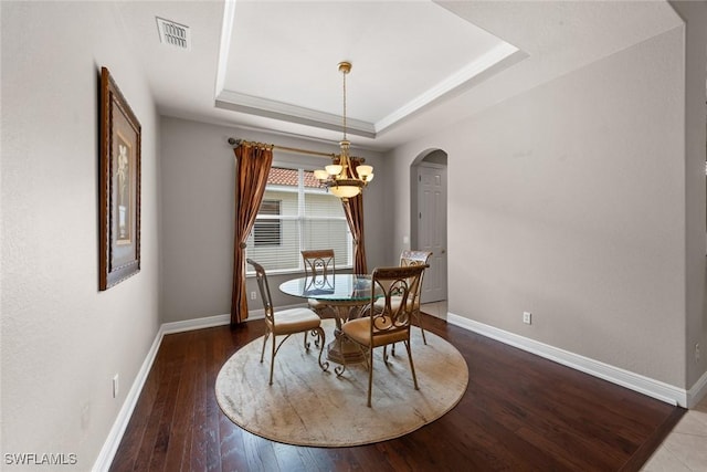 dining room with arched walkways, visible vents, baseboards, wood-type flooring, and a raised ceiling