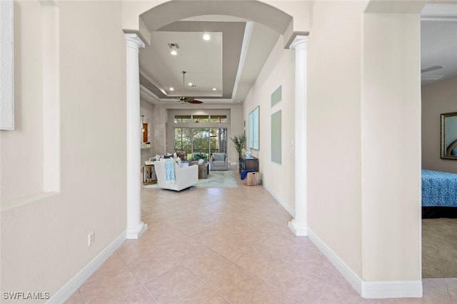 hallway featuring arched walkways, a raised ceiling, decorative columns, and baseboards