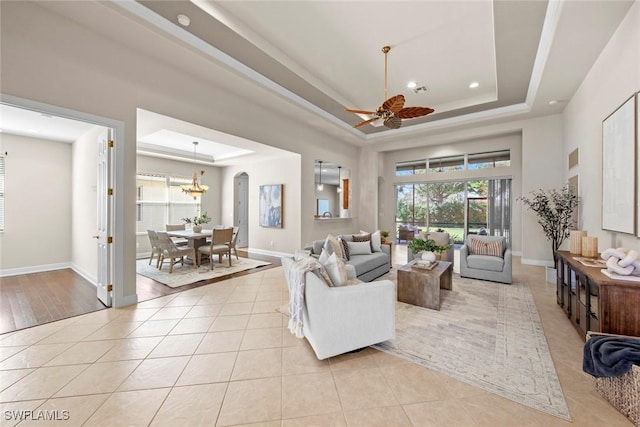 living room with ceiling fan with notable chandelier, a raised ceiling, baseboards, and light tile patterned floors