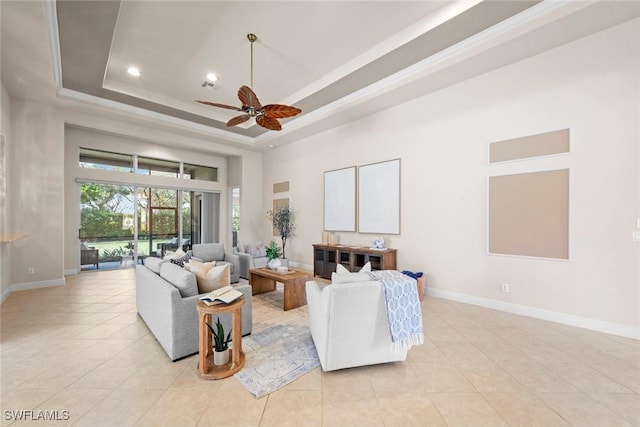 living area with a ceiling fan, a raised ceiling, and baseboards