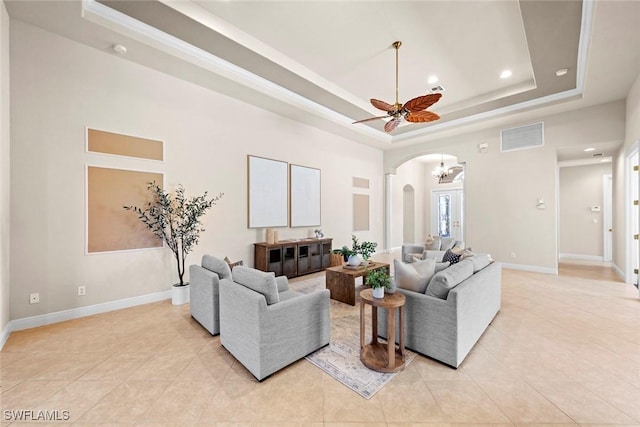 living area with arched walkways, baseboards, a tray ceiling, and light tile patterned flooring