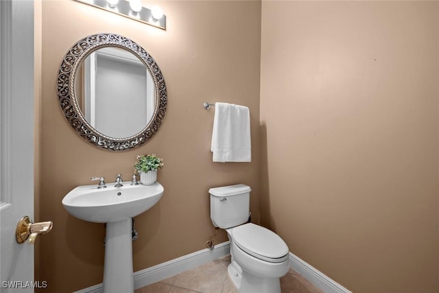 bathroom featuring toilet, baseboards, a sink, and tile patterned floors