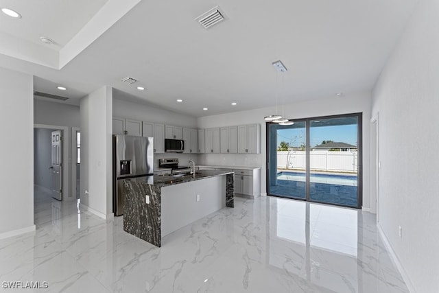 kitchen featuring dark stone counters, gray cabinetry, stainless steel appliances, a kitchen island with sink, and pendant lighting