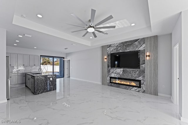 living room featuring a high end fireplace, a tray ceiling, ceiling fan, and sink