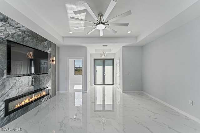 unfurnished living room featuring a raised ceiling, ceiling fan, a fireplace, and french doors