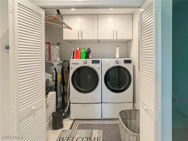 laundry area featuring washing machine and clothes dryer, light tile patterned floors, and cabinets