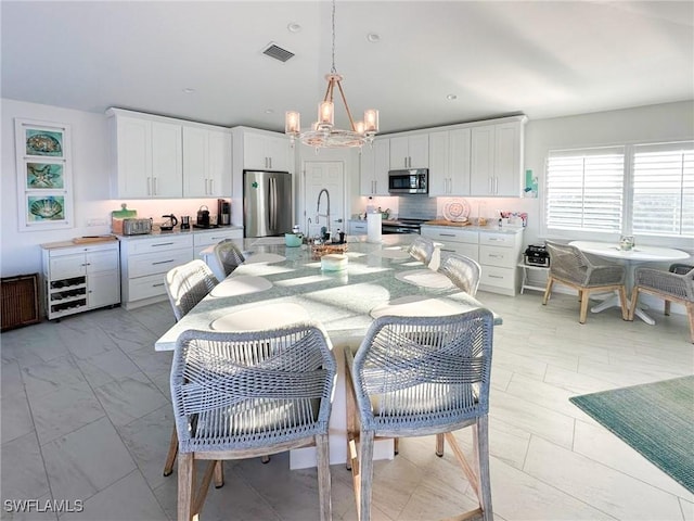 kitchen with white cabinets, decorative light fixtures, decorative backsplash, and stainless steel appliances