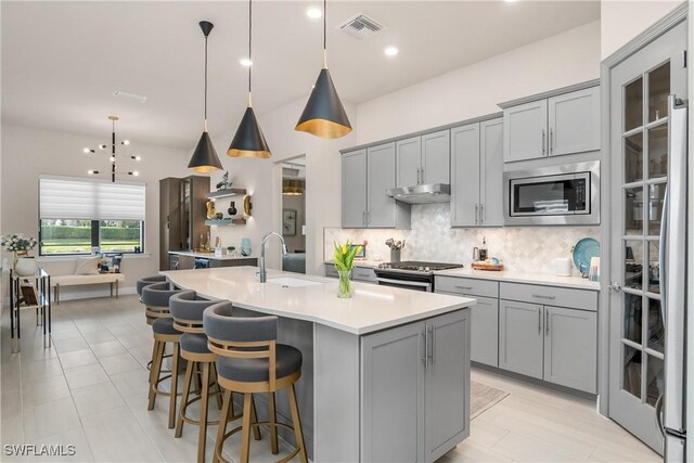 kitchen featuring appliances with stainless steel finishes, sink, a center island with sink, decorative light fixtures, and gray cabinets