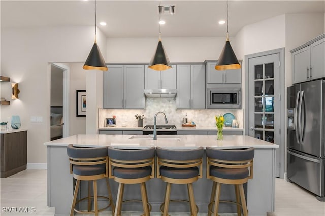 kitchen with decorative backsplash, pendant lighting, stainless steel appliances, and a center island with sink