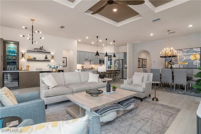 living room with ceiling fan with notable chandelier, wine cooler, coffered ceiling, and light tile patterned flooring