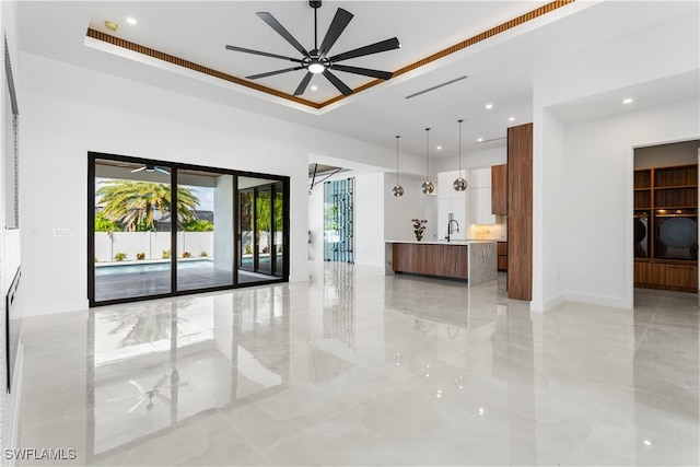 interior space featuring a tray ceiling, ceiling fan, sink, pendant lighting, and a kitchen island