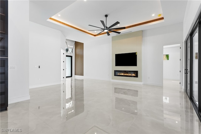 unfurnished living room with ceiling fan and a tray ceiling