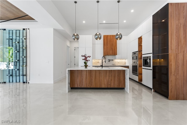 kitchen featuring decorative backsplash, sink, white cabinetry, hanging light fixtures, and an island with sink