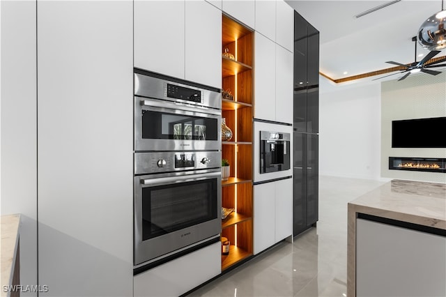 kitchen with white cabinets, ceiling fan, light stone countertops, and double oven