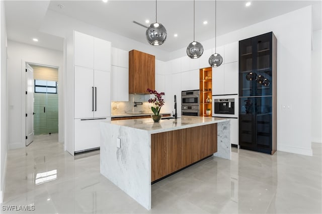 kitchen with a large island with sink, white cabinetry, double oven, and pendant lighting