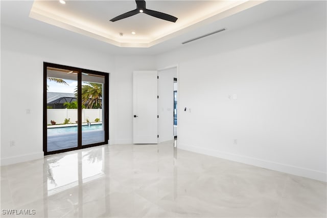 empty room with ceiling fan and a raised ceiling