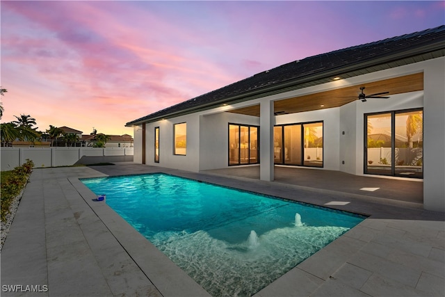 pool at dusk featuring ceiling fan and a patio