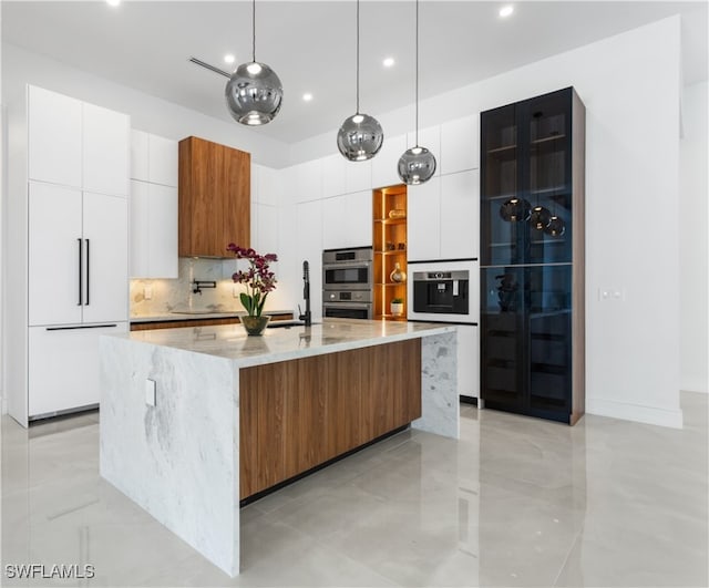 kitchen with white cabinets, a large island with sink, stainless steel double oven, and decorative light fixtures