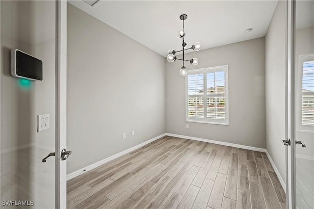 unfurnished room with french doors, light hardwood / wood-style flooring, and a chandelier