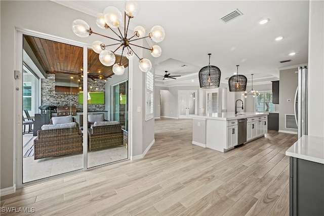 kitchen featuring ceiling fan with notable chandelier, a kitchen island with sink, sink, pendant lighting, and white cabinets