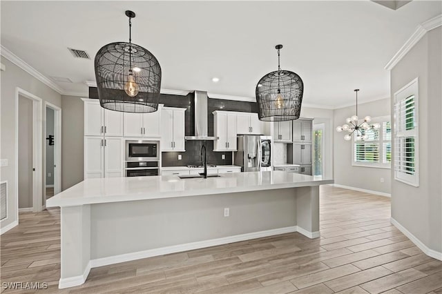 kitchen with a spacious island, wall chimney exhaust hood, decorative backsplash, appliances with stainless steel finishes, and a notable chandelier