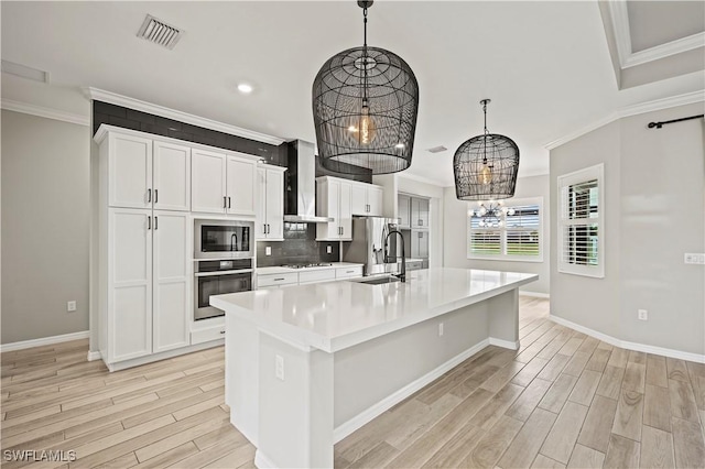 kitchen with a center island with sink, a notable chandelier, wall chimney range hood, and appliances with stainless steel finishes