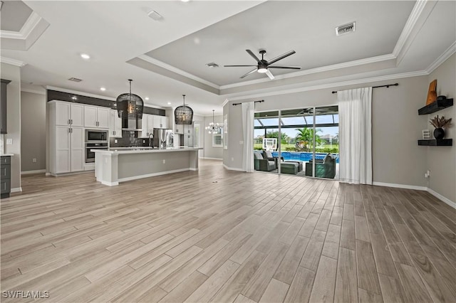 unfurnished living room featuring ceiling fan with notable chandelier, a tray ceiling, and ornamental molding