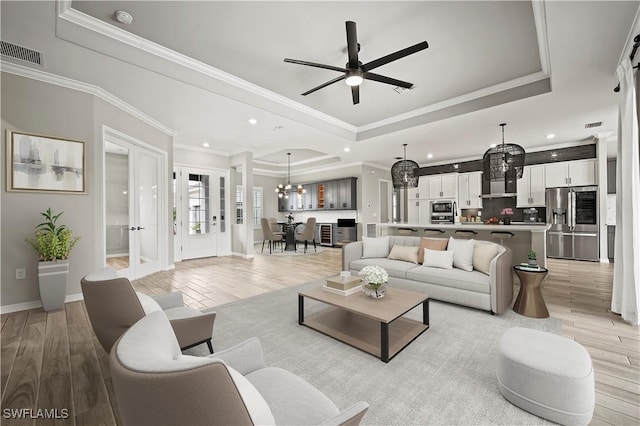 living room with ceiling fan with notable chandelier, ornamental molding, and a tray ceiling