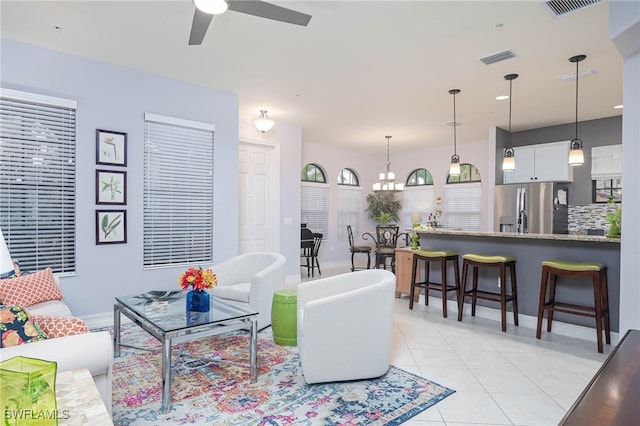 tiled living room with ceiling fan with notable chandelier