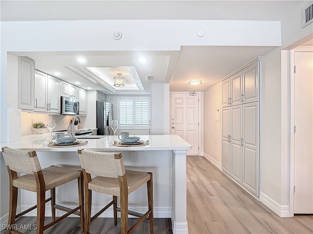 kitchen featuring a breakfast bar, kitchen peninsula, sink, light wood-type flooring, and appliances with stainless steel finishes