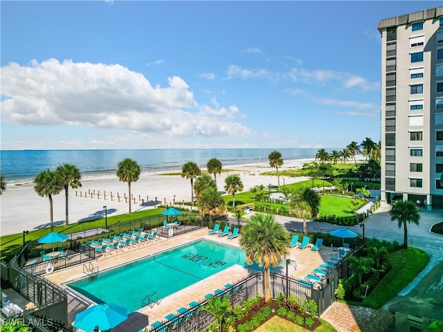 view of swimming pool with a patio area, a water view, and a view of the beach