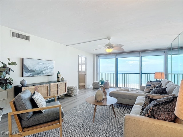 living room with ceiling fan, expansive windows, wood-type flooring, and a water view