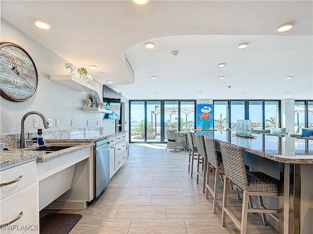 kitchen featuring white cabinetry, stainless steel dishwasher, light stone counters, expansive windows, and sink