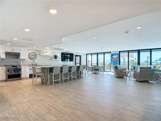 interior space with light stone countertops, white cabinetry, a wall of windows, double oven range, and a breakfast bar