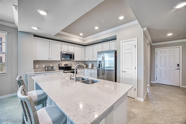 kitchen with light stone countertops, sink, stainless steel appliances, an island with sink, and white cabinets