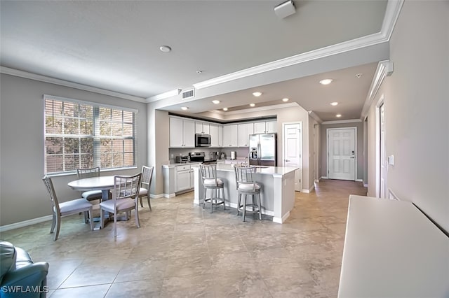 kitchen featuring appliances with stainless steel finishes, ornamental molding, a breakfast bar, white cabinets, and a kitchen island