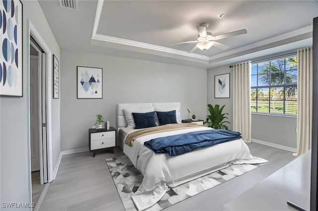 bedroom with a raised ceiling, ceiling fan, ornamental molding, and light wood-type flooring