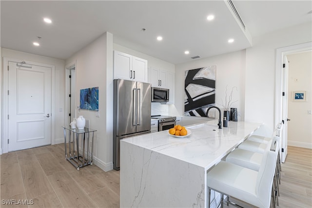 kitchen with a breakfast bar area, white cabinetry, light stone countertops, and appliances with stainless steel finishes