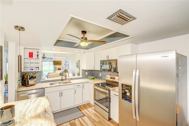 kitchen with white cabinets, appliances with stainless steel finishes, a tray ceiling, decorative light fixtures, and light stone counters