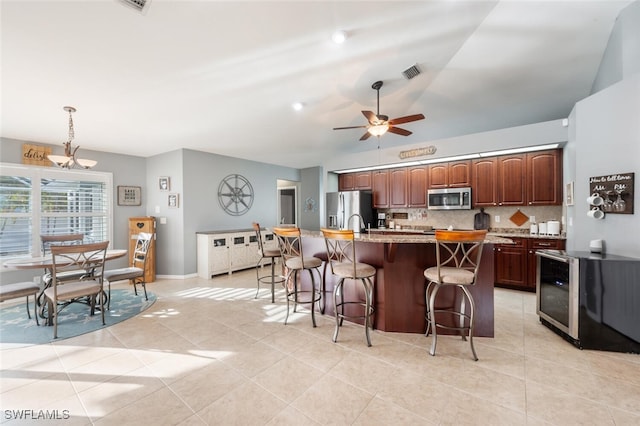 kitchen with pendant lighting, tasteful backsplash, a kitchen island with sink, appliances with stainless steel finishes, and a kitchen breakfast bar