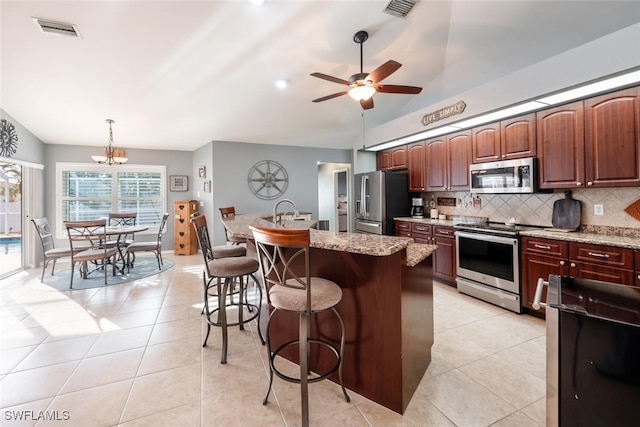 kitchen featuring stainless steel appliances, vaulted ceiling, tasteful backsplash, hanging light fixtures, and a kitchen island with sink