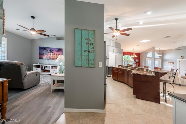 kitchen featuring sink, lofted ceiling, a kitchen bar, an island with sink, and light stone countertops