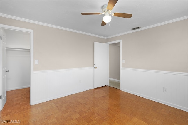 unfurnished bedroom with a closet, light parquet floors, a walk in closet, crown molding, and ceiling fan