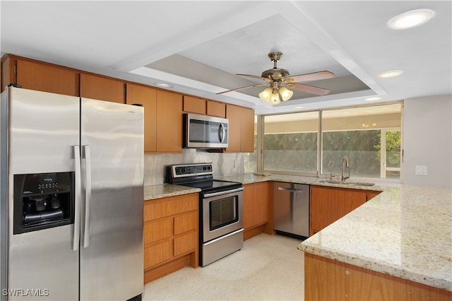 kitchen with sink, appliances with stainless steel finishes, light stone countertops, backsplash, and a tray ceiling