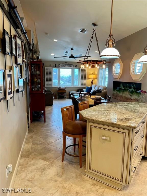 kitchen with light stone countertops, a kitchen breakfast bar, ceiling fan, decorative light fixtures, and a kitchen island