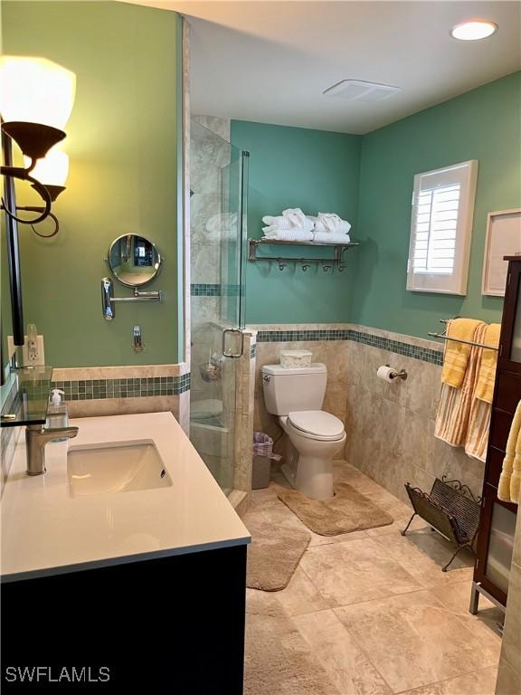 full bathroom with a stall shower, toilet, a wainscoted wall, vanity, and tile walls