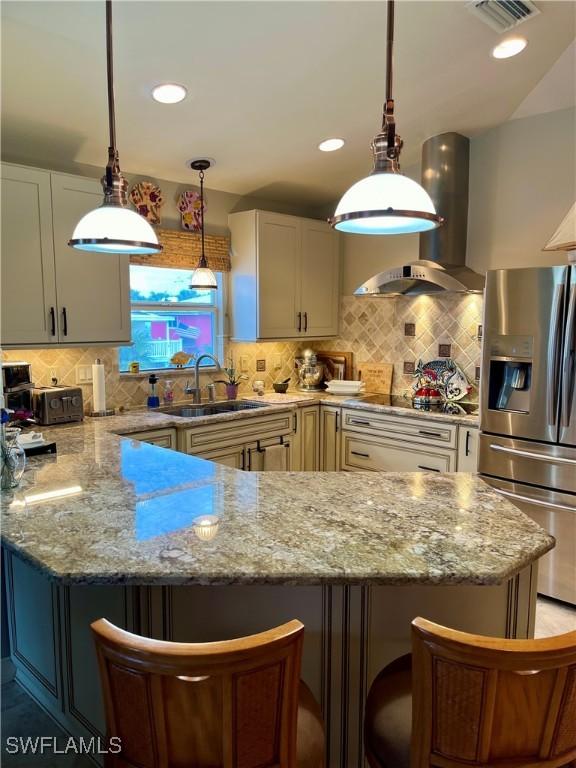 kitchen with sink, light stone countertops, appliances with stainless steel finishes, island range hood, and a kitchen bar